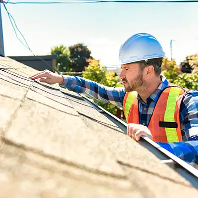 Worker with orange vest and hard hat inspecting a residential roof